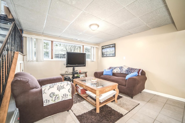 tiled living area featuring a paneled ceiling, stairway, and baseboards