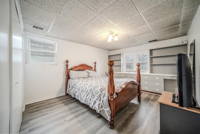 bedroom with a paneled ceiling, visible vents, baseboards, and wood finished floors