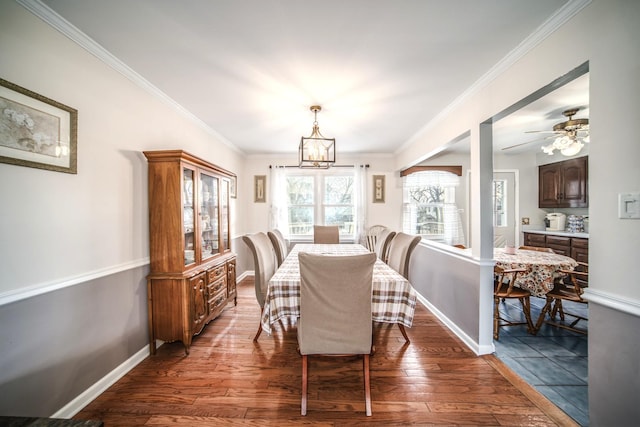 dining space featuring crown molding, ceiling fan with notable chandelier, dark wood finished floors, and baseboards