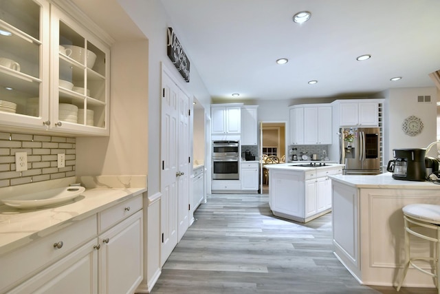 kitchen with light wood-style flooring, recessed lighting, stainless steel appliances, white cabinets, and glass insert cabinets