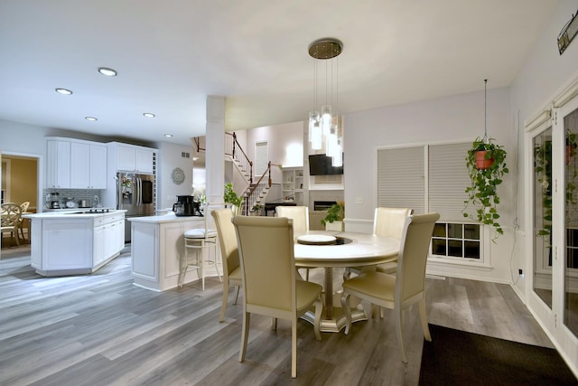 dining space featuring stairs, light wood-type flooring, a fireplace, and recessed lighting