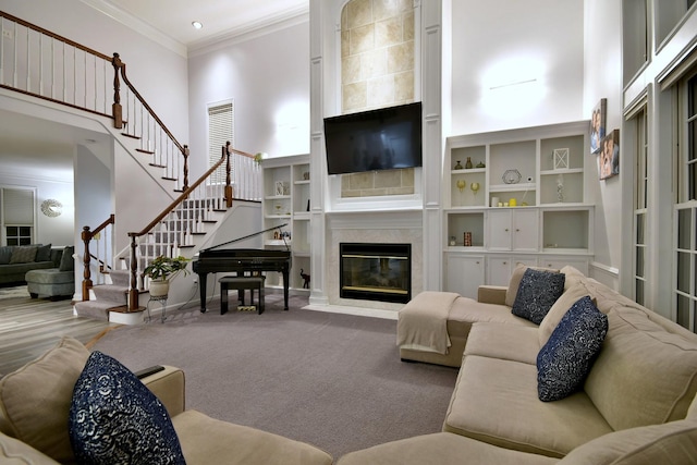 carpeted living room featuring built in shelves, a fireplace, stairway, a towering ceiling, and ornamental molding