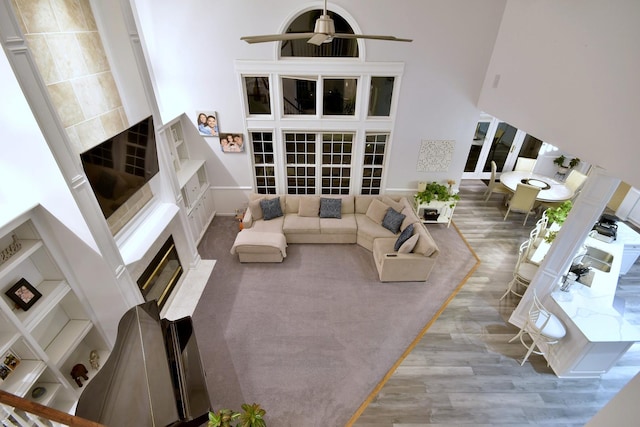 living area with a towering ceiling, a ceiling fan, wood finished floors, and a glass covered fireplace