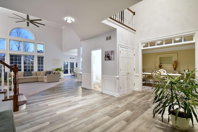 interior space with light wood-style flooring, a towering ceiling, visible vents, stairway, and wainscoting