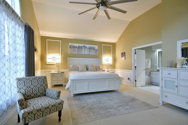 bedroom featuring light carpet, connected bathroom, a wainscoted wall, high vaulted ceiling, and a decorative wall