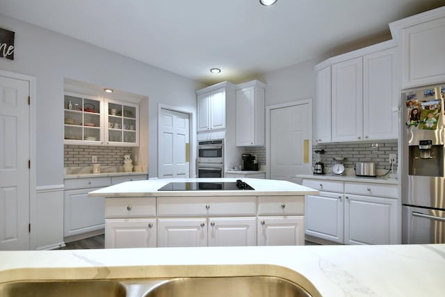 kitchen featuring tasteful backsplash, white cabinets, glass insert cabinets, stainless steel appliances, and light countertops