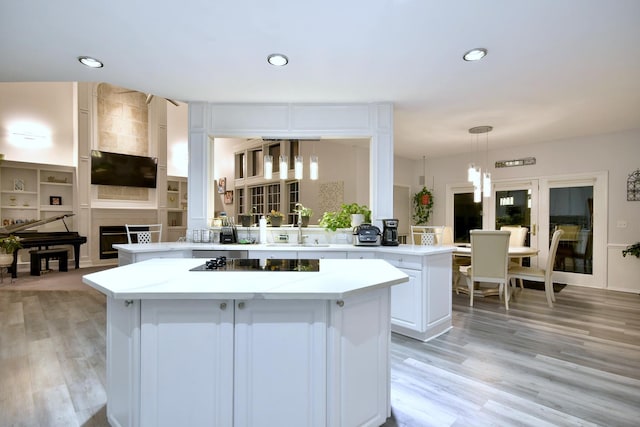 kitchen with light wood-type flooring, a peninsula, black electric cooktop, and a center island