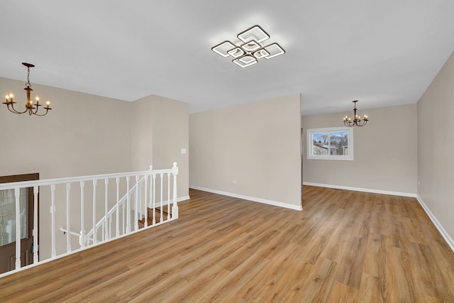 spare room with light wood-style flooring, baseboards, and an inviting chandelier