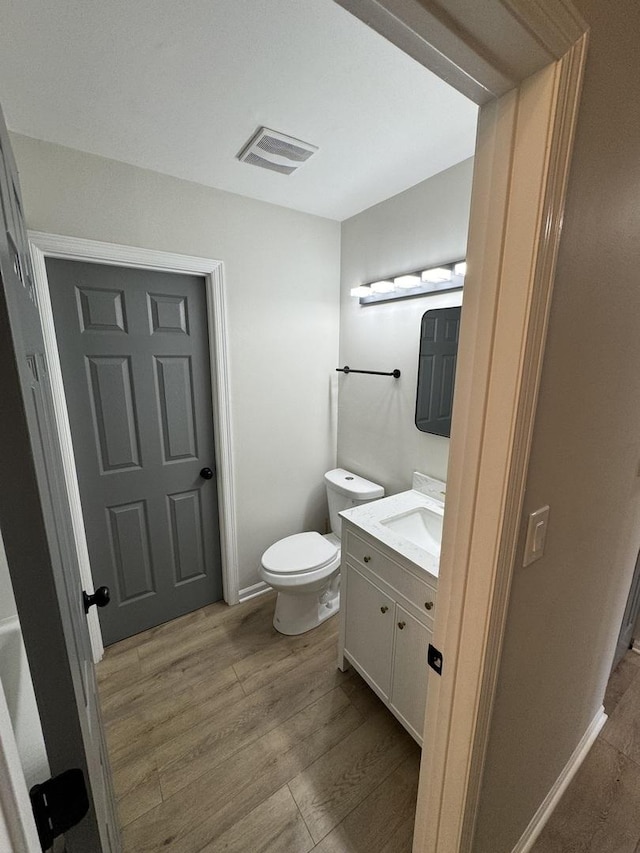 bathroom featuring visible vents, toilet, vanity, wood finished floors, and baseboards