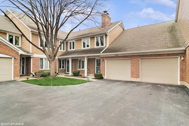 multi unit property with aphalt driveway, brick siding, a chimney, a shingled roof, and an attached garage