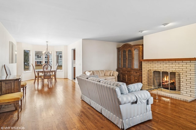 living room with a brick fireplace, a chandelier, and wood finished floors