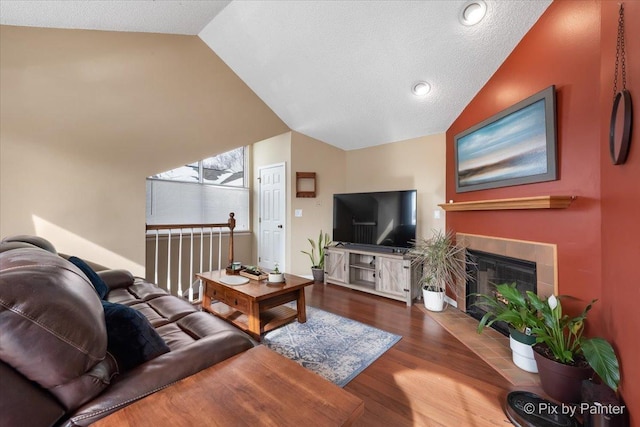 living area featuring vaulted ceiling, a textured ceiling, a tiled fireplace, and dark wood finished floors