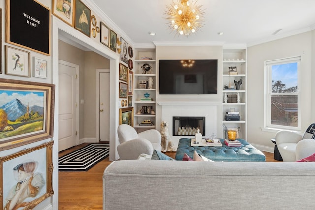 living room with built in features, crown molding, a fireplace, an inviting chandelier, and wood finished floors