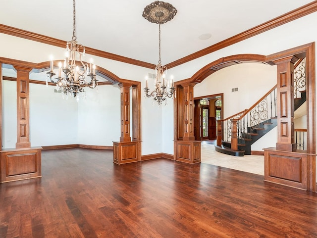 unfurnished dining area with arched walkways, wood finished floors, decorative columns, and an inviting chandelier