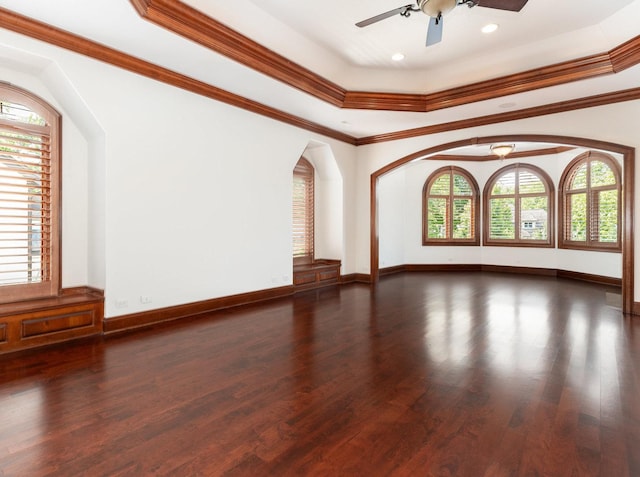 unfurnished room featuring baseboards, a raised ceiling, a ceiling fan, ornamental molding, and wood finished floors