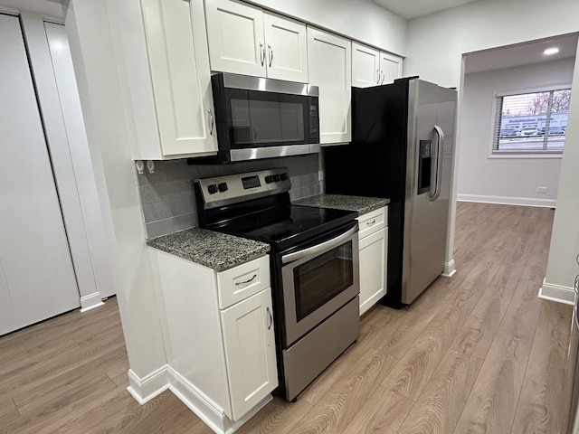 kitchen with stainless steel appliances, light wood-style flooring, dark stone countertops, and white cabinetry