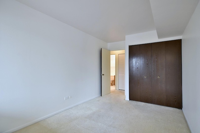 unfurnished bedroom with a closet, light carpet, and baseboards