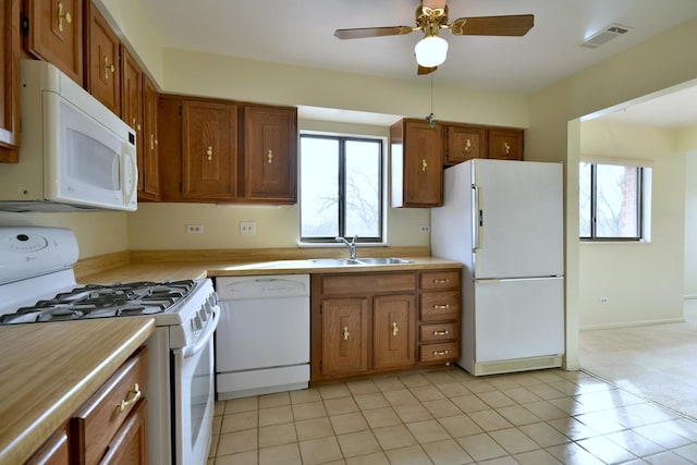 kitchen featuring white appliances, brown cabinets, light countertops, a healthy amount of sunlight, and a sink