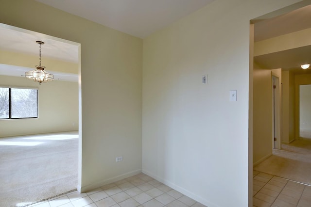 spare room with a chandelier, light colored carpet, baseboards, and light tile patterned flooring