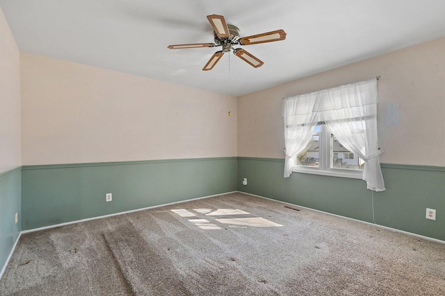 carpeted empty room featuring a ceiling fan, a wainscoted wall, and visible vents