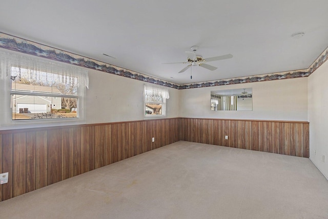 empty room with carpet floors, plenty of natural light, wooden walls, and wainscoting