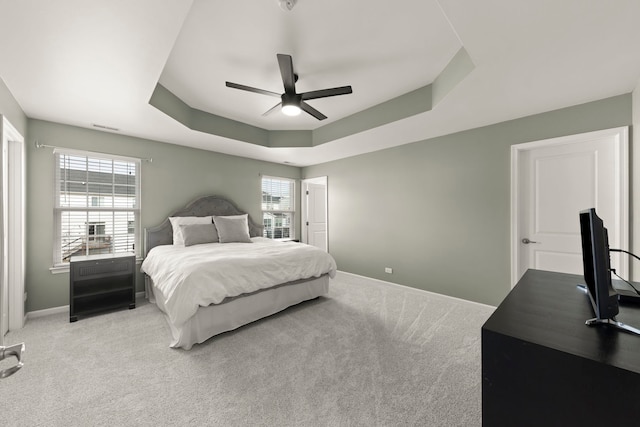 bedroom featuring a raised ceiling, multiple windows, light carpet, and baseboards