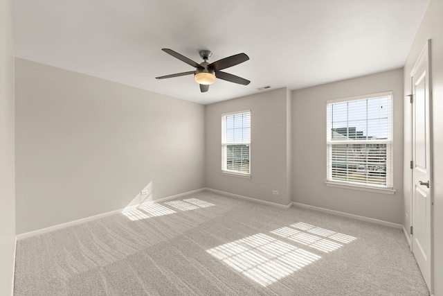 unfurnished room with ceiling fan, light colored carpet, visible vents, and baseboards