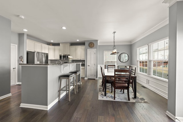 kitchen with dark stone counters, ornamental molding, appliances with stainless steel finishes, decorative light fixtures, and a kitchen bar