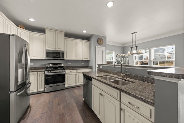 kitchen with dark stone counters, ornamental molding, hanging light fixtures, stainless steel appliances, and a sink