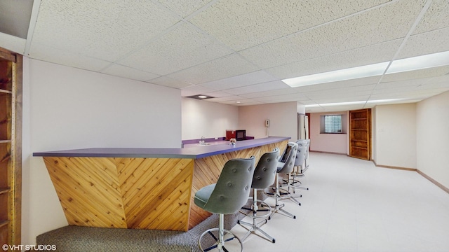 bar with bar, a drop ceiling, and baseboards