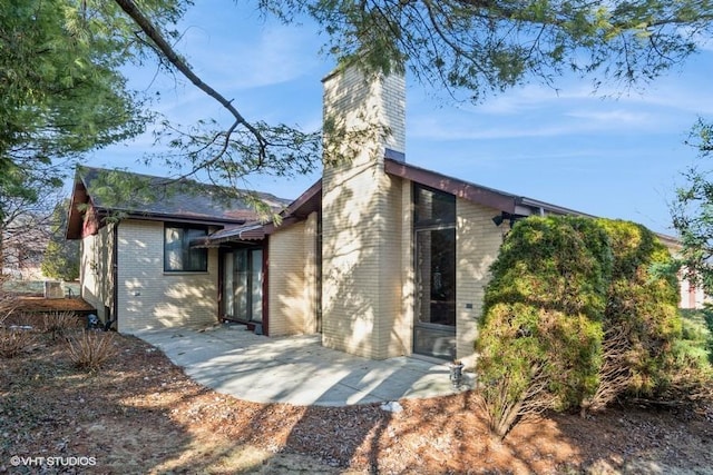 exterior space featuring brick siding, a patio, and a chimney