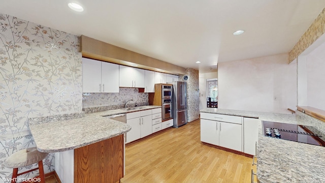 kitchen featuring a peninsula, stainless steel appliances, a sink, and wallpapered walls