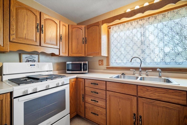 kitchen featuring stainless steel microwave, light countertops, white gas range oven, brown cabinets, and a sink