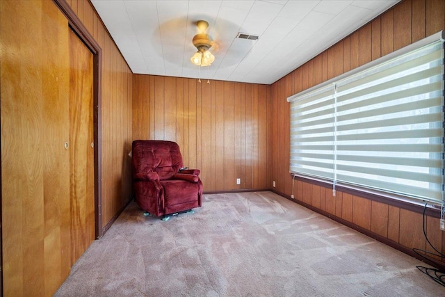 unfurnished room featuring visible vents, carpet flooring, a ceiling fan, and wood walls