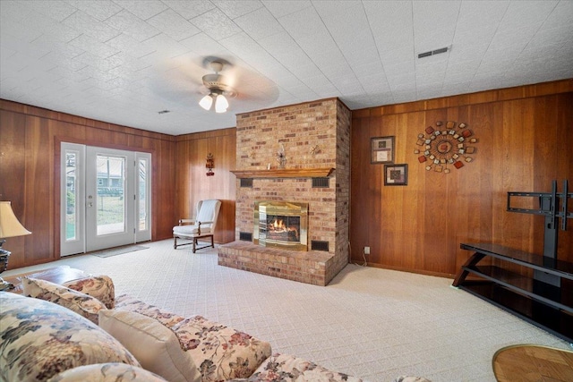 living room with visible vents, wooden walls, carpet, a fireplace, and ceiling fan