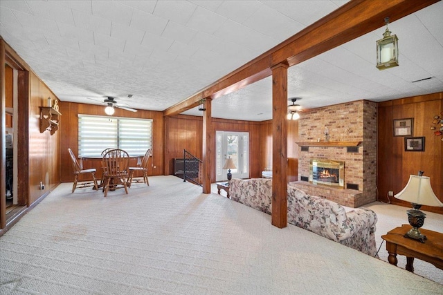 dining area with wood walls, a brick fireplace, a ceiling fan, and carpet floors