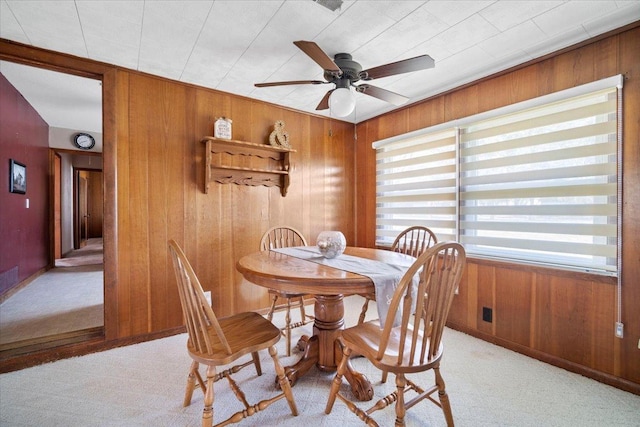 dining area featuring light colored carpet, ceiling fan, and wooden walls