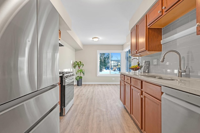 kitchen featuring light stone counters, a sink, appliances with stainless steel finishes, light wood finished floors, and tasteful backsplash