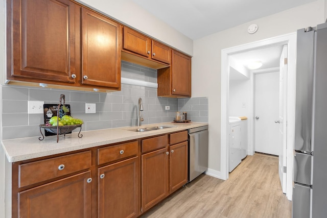 kitchen with a sink, appliances with stainless steel finishes, brown cabinets, and washer and dryer