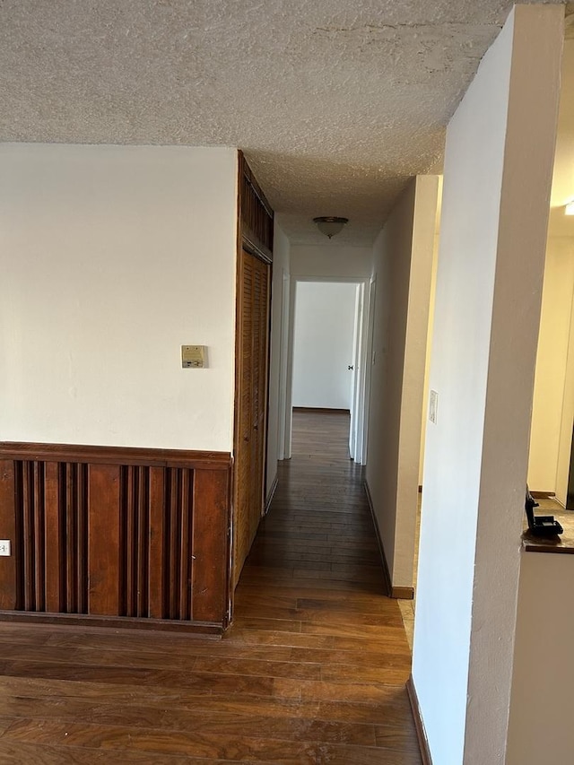 hallway with a wainscoted wall, a textured ceiling, and dark wood-style flooring