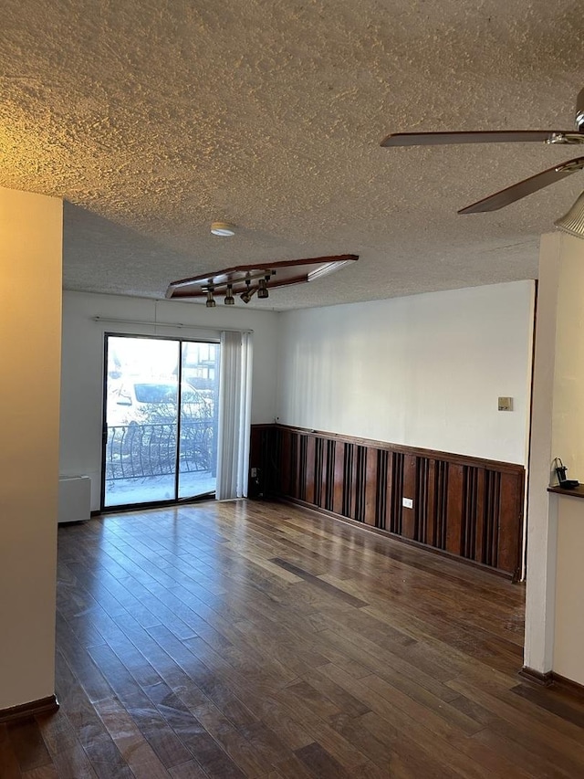 unfurnished room with dark wood-style floors, ceiling fan, a textured ceiling, and wainscoting