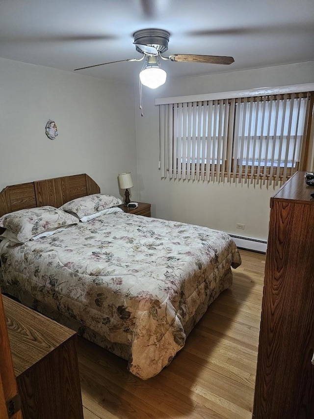 bedroom featuring a ceiling fan, wood finished floors, and a baseboard heating unit