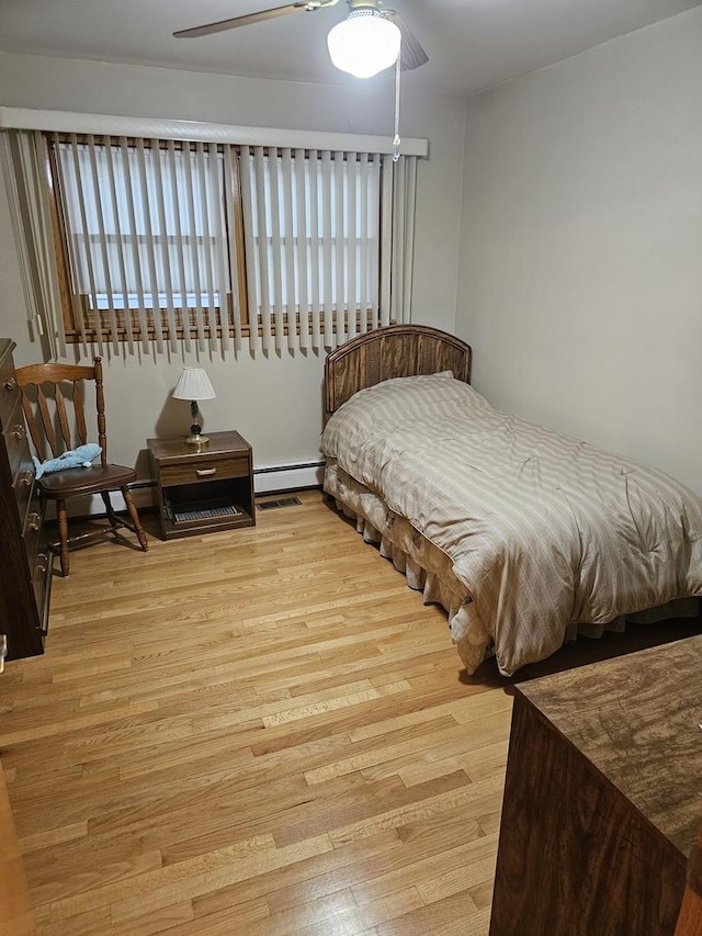 bedroom featuring ceiling fan, baseboard heating, and wood finished floors