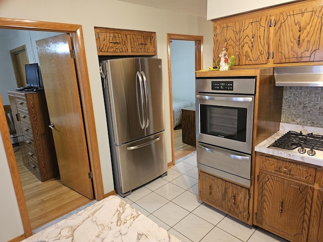 kitchen with a warming drawer, brown cabinets, appliances with stainless steel finishes, and light countertops