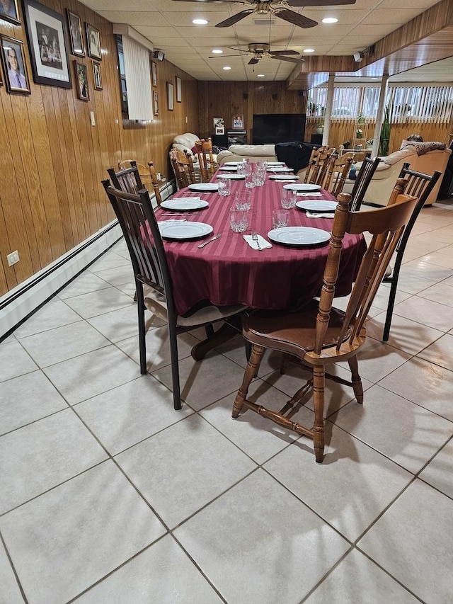 dining room featuring a drop ceiling, wooden walls, baseboard heating, and ceiling fan