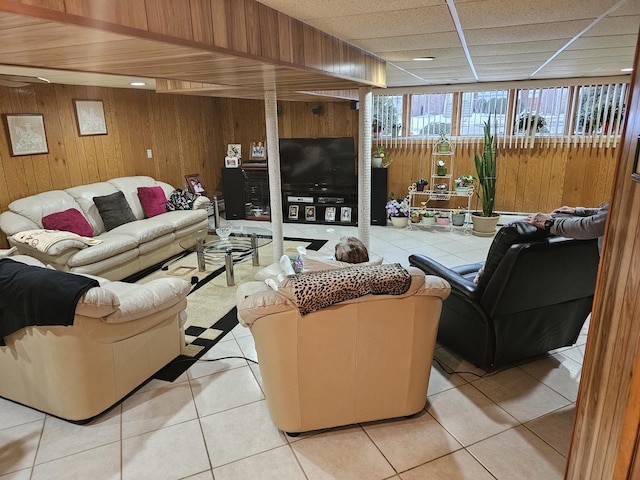 living room featuring wooden walls, light tile patterned floors, and a paneled ceiling