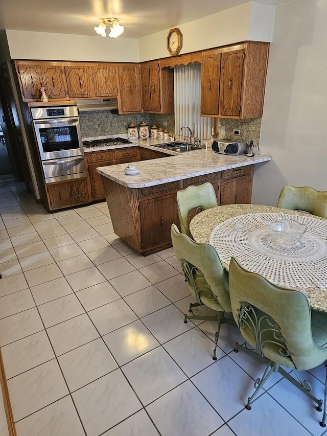 kitchen with a warming drawer, a sink, stainless steel appliances, a peninsula, and light tile patterned floors