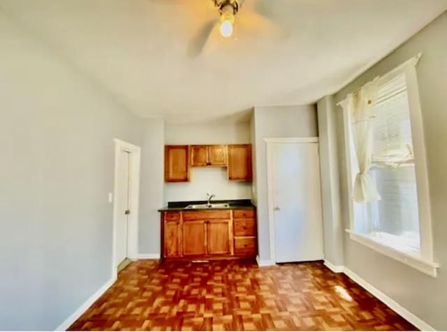 kitchen with baseboards, brown cabinetry, dark countertops, ceiling fan, and a sink