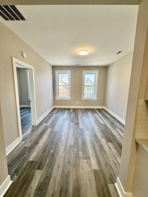 unfurnished room featuring dark wood finished floors, visible vents, and baseboards