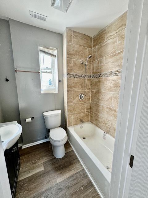 full bath with toilet, wood finished floors, visible vents, vanity, and tub / shower combination